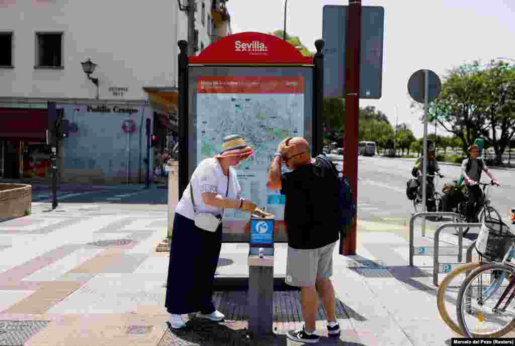 Пар се лади со вода од јавна фонтана во Севиља, 29 јуни.