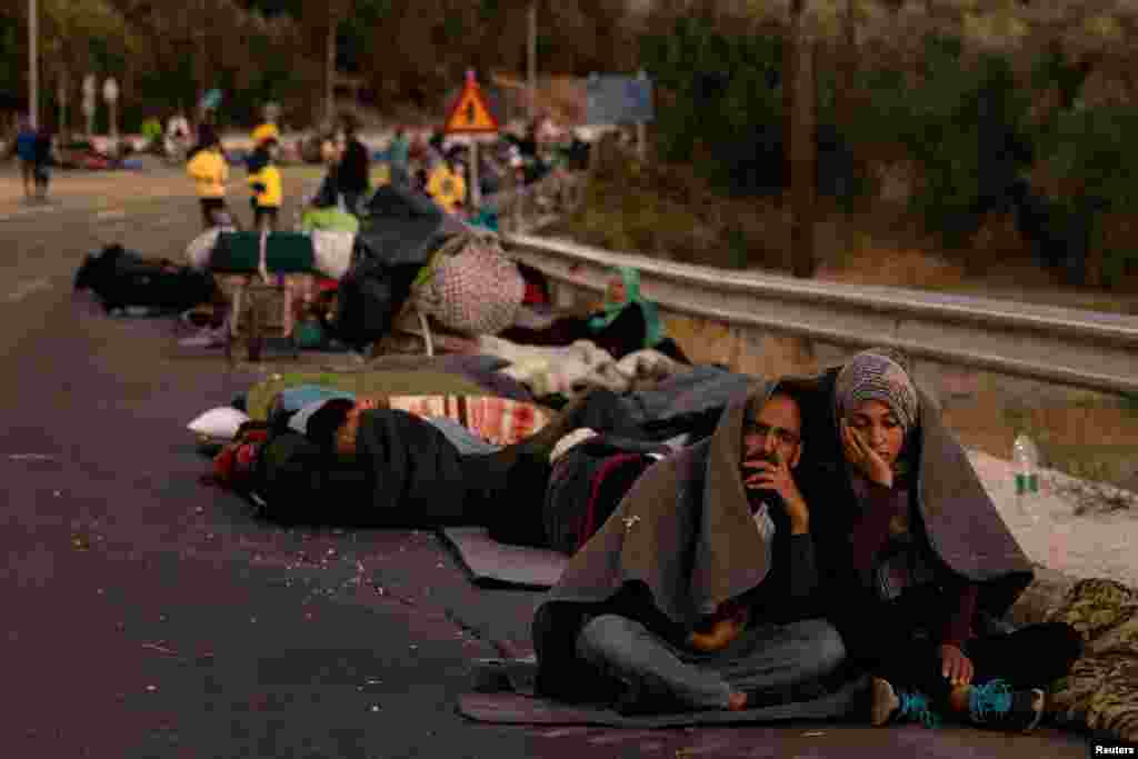 Një çift i mbështjellur shihet duke shikur migrantë tjerë që kanë mbetur të pastrehë.