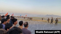 Afganii (stânga) se adună pe aeroport în vreme ce militarii americani fac de gardă, Kabul, 16 august 2021.