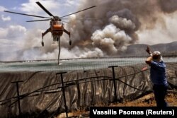 Egy helikoptert töltenek fel vízzel Szpaszovuninál, Korinthosz közelében, Görögországban 2021. július 23-án