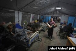 Një nënë duke bartur fëmijën e saj në një tendë për trajtimin e pacientëve, në oborin e spitalit Shifa.