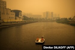 Egy pár csónakázik, miközben a közeli erdőtüzekből származó füst narancsszínűre festi az eget Jakutszk felett a szibériai Szaha Köztársaságban 2021. július 27-én