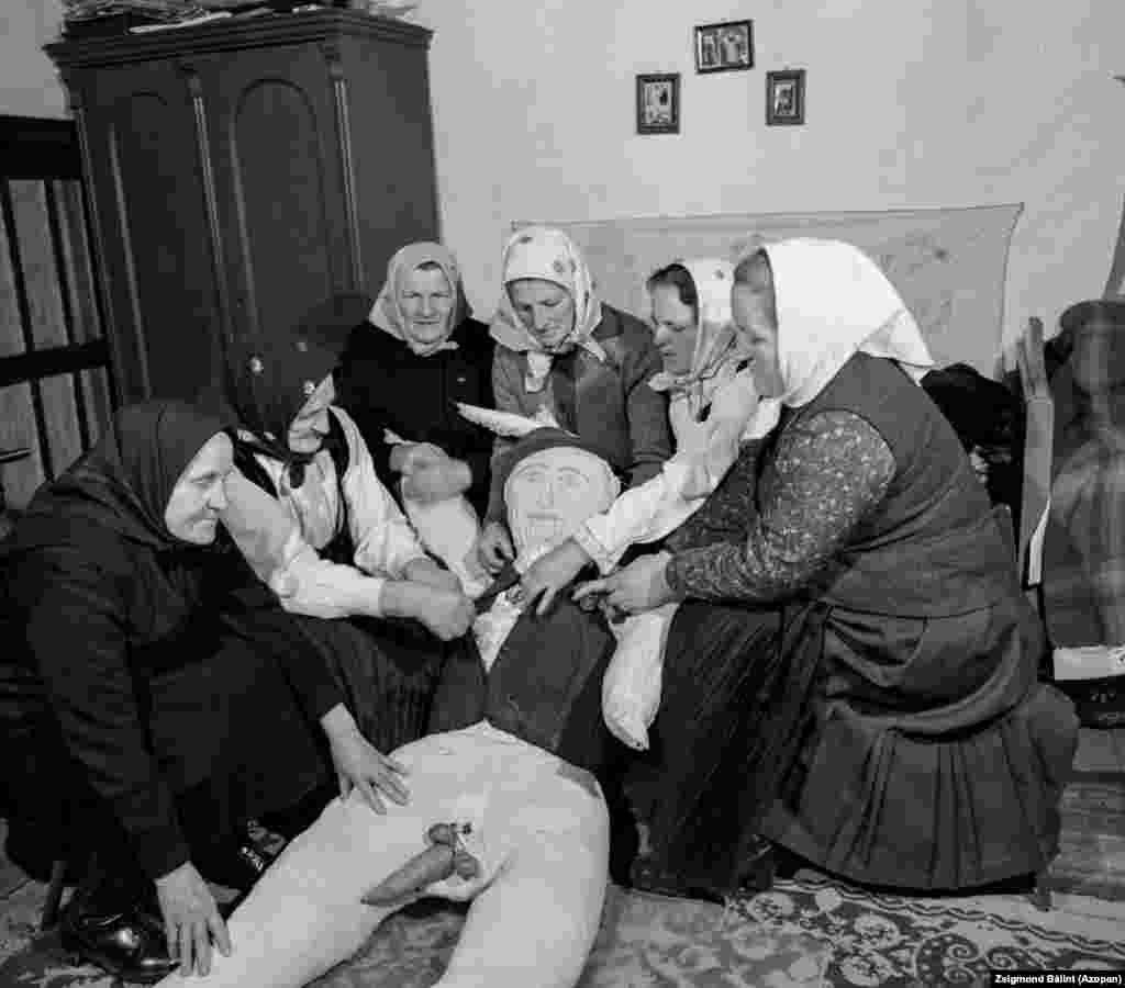 Femeile din satul Ocna de Jos pregătesc un manechin dotat cu organe genitale vegetale pentru un carnaval tradițional în 1983. Manechinul, cunoscut sub numele de &bdquo;bețivul satului&rdquo;, este defilat prin sat în Miercurea Cenușii pentru a marca sfârșitul Postului Mare, înainte de a fi ars. Tradiția este încă foarte vie și astăzi. &nbsp;