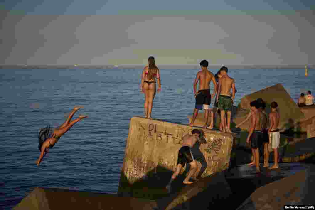 Млади луѓе скокаат во вода од карпа покрај морето, Барселона, Шпанија, на 29 јуни.